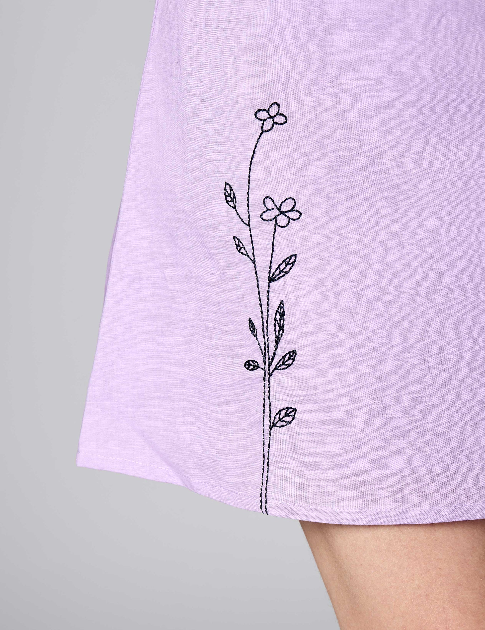Close-up of clean black thread embroidery on the hem of a lilac linen-cotton sustainable dress.