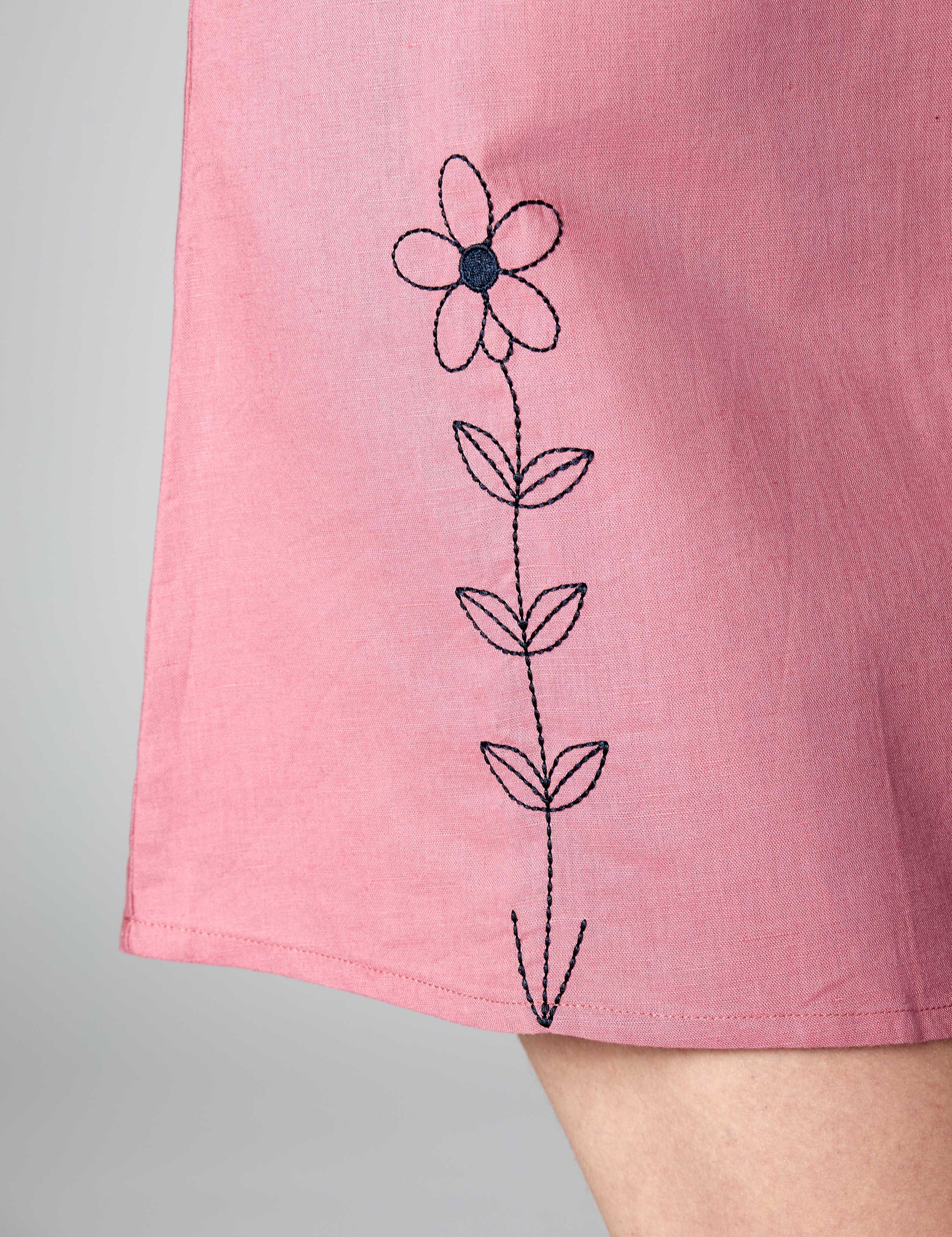 Detailed shot of black thread embroidery on the hem of a pink 3/4 sleeve linen-cotton dress.