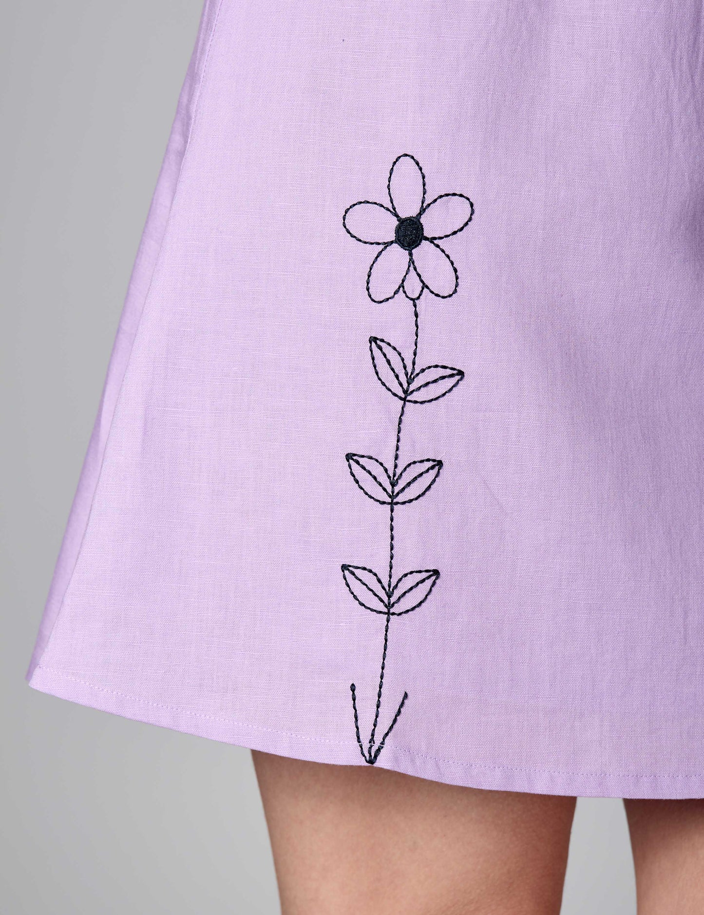 Detailed shot of black thread embroidery on the hem of a lilac 3/4 sleeve sustainable dress.