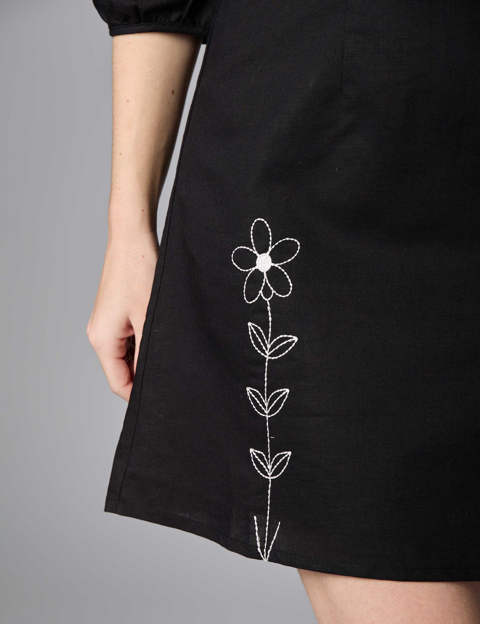 Detailed shot of silver thread embroidery on the hem of a classic black 3/4 sleeve summer dress.