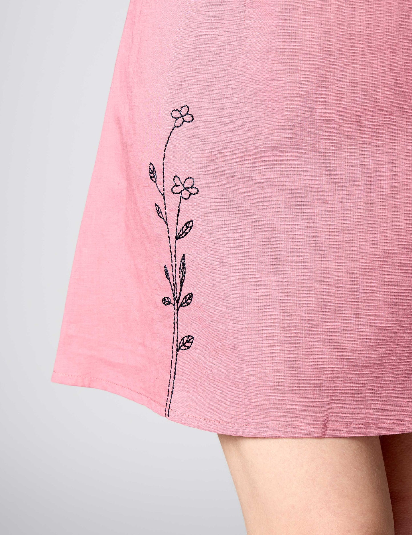 Detailed shot of durable black thread embroidery on the hem of a pink linen-cotton summer dress.